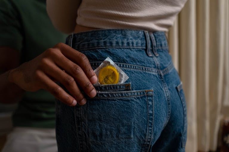 Condom being placed into denim jeans pocket, emphasizing safe sex and contraceptive use. | Edging, Exercise and Other Ways to Prevent Premature Ejaculation