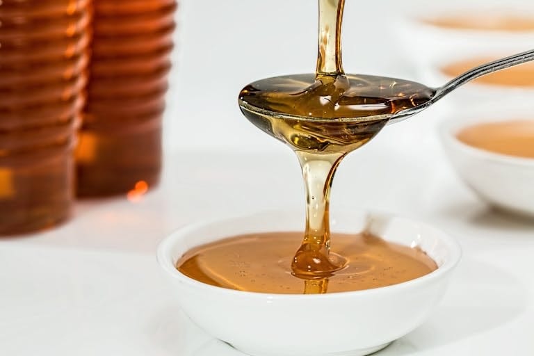 Delicious honey pouring slowly from a spoon into a white bowl, highlighting its golden hue and viscosity. | Ditch Sugar: The 10 Best Healthy Sugar Alternatives Ranked