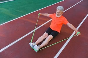 Elderly man exercising on a track with a resistance band, showcasing strength and fitness. | A Physical Therapist’s Top Resistance Band Exercises to Stop Joint Pain in Its Tracks