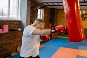 Elderly man in a gym boxing a punching bag for exercise and fitness.