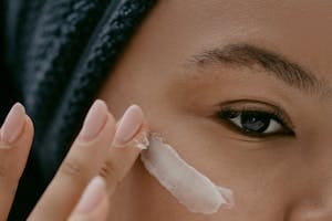 Extreme close-up of a woman applying cream to her cheek for healthy skin care. | Best Eye Creams for Dry Skin