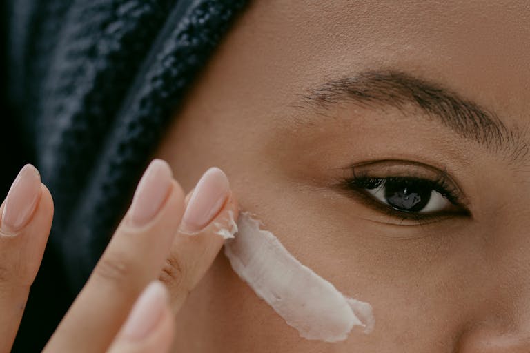 Extreme close-up of a woman applying cream to her cheek for healthy skin care. | Best Eye Creams for Dry Skin