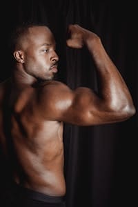 Powerful pose of a shirtless African American man flexing his bicep. | 5 Unique Exercises You Haven’t Tried Yet to Build Strong, Muscular Arms | 5 Low-Impact Moves to Strengthen Your Whole Body—No Jumping Needed