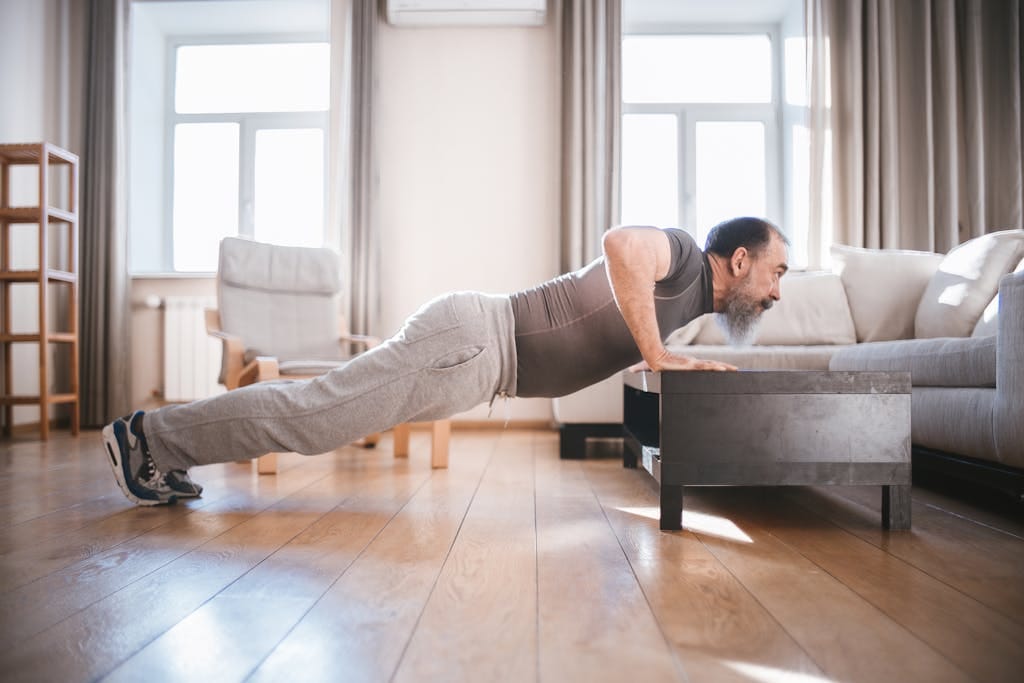 Senior man exercising at home with push-ups on a wooden floor, promoting healthy lifestyle. | 65 and Crushing It: The Workout Routine That Keeps Me in the Best Shape of My Life