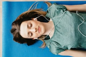 Young woman meditating with closed eyes on a yoga mat, listening to music. | What Is Yoga Nidra? I Tried It for 10 Days to See If It Could Transform My Sleep