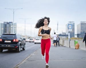A fit woman with curly hair runs on a city street, enjoying music and staying healthy. | Stop Wasting Your Mornings: 5 Fat-Burning Morning Habits That Melt Belly Fat Fast (Backed by Science)