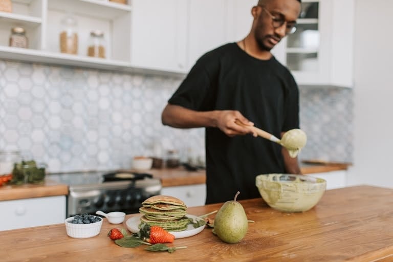 A man in a kitchen making green pancakes with fresh fruits. Healthy home cooking concept. | Want Better Gut Health and More Protein? A Doctor Reveals the Surprisingly Simple Way to Get Both