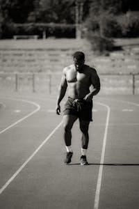 A muscular male athlete walking on a track in a black and white photograph. | Ditch the Treadmill: The 15-Minute Walking Workout That Burns Fat Without Joint Pain