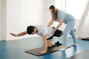 A physiotherapist guides a patient's exercise on a mat in a Vilnius gym. | 5 Exercises That Fix Posture Better Than a Chiropractor (No Equipment!)