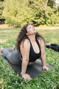 A plus size woman doing yoga on a mat outdoors in a green park setting. | 10 Effortless Yoga Poses That Help Plus-Size Seniors Build Strength & Confidence—No Flexibility Needed