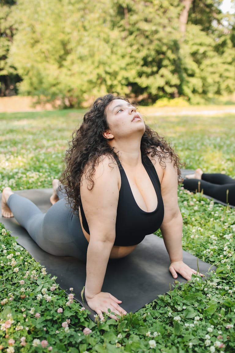 A plus size woman doing yoga on a mat outdoors in a green park setting. | 10 Effortless Yoga Poses That Help Plus-Size Seniors Build Strength & Confidence—No Flexibility Needed