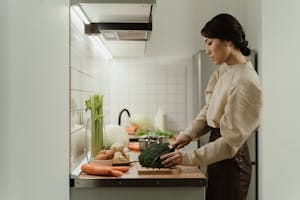 A woman chops broccoli on a kitchen counter with various fresh vegetables around. | How to Eat More Protein Without Wrecking Your Gut or Missing Other Nutrients