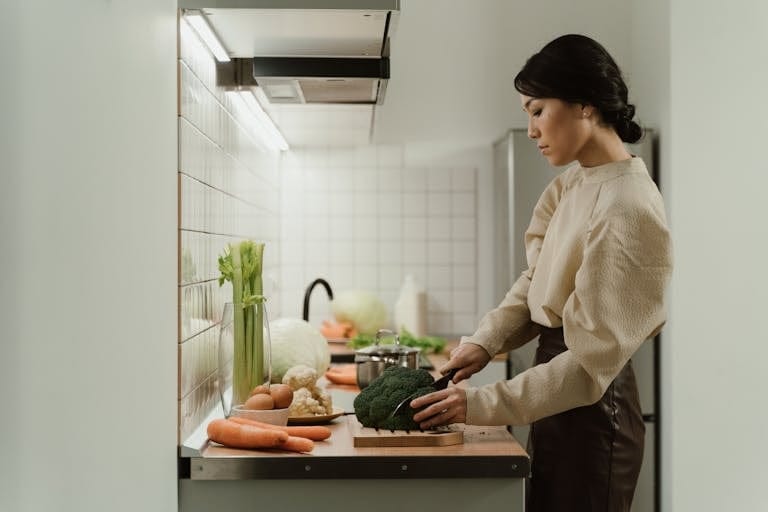 A woman chops broccoli on a kitchen counter with various fresh vegetables around. | How to Eat More Protein Without Wrecking Your Gut or Missing Other Nutrients