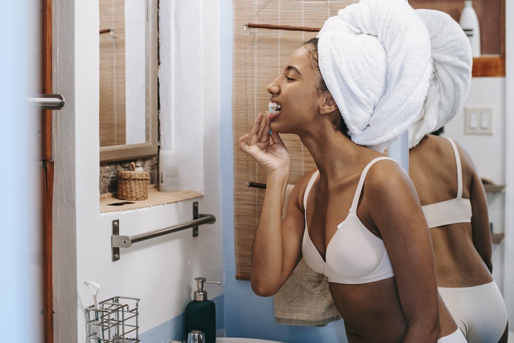 A young woman in a bathroom flossing her teeth with a towel wrapped around her head, promoting oral hygiene. | Dentists Say These 10 Habits Can Save Your Gums—Are You Doing Them?