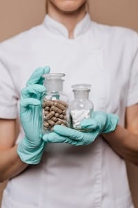 Close-up of a healthcare worker holding bottles of capsules and tablets wearing gloves. | Stop Wasting Your Cash: A Pharmacist Says These 5 Supplements Do Nothing for Your Health