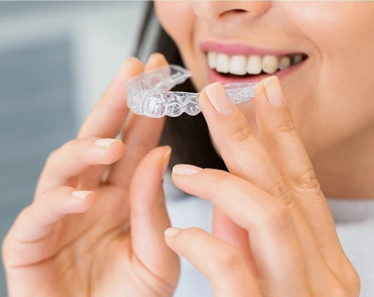 Close-up of a woman holding a clear dental aligner, showcasing dental health and a bright smile. | 8 Proven Ways to Straighten Your Teeth Without Braces (Dentists Swear by #3)
