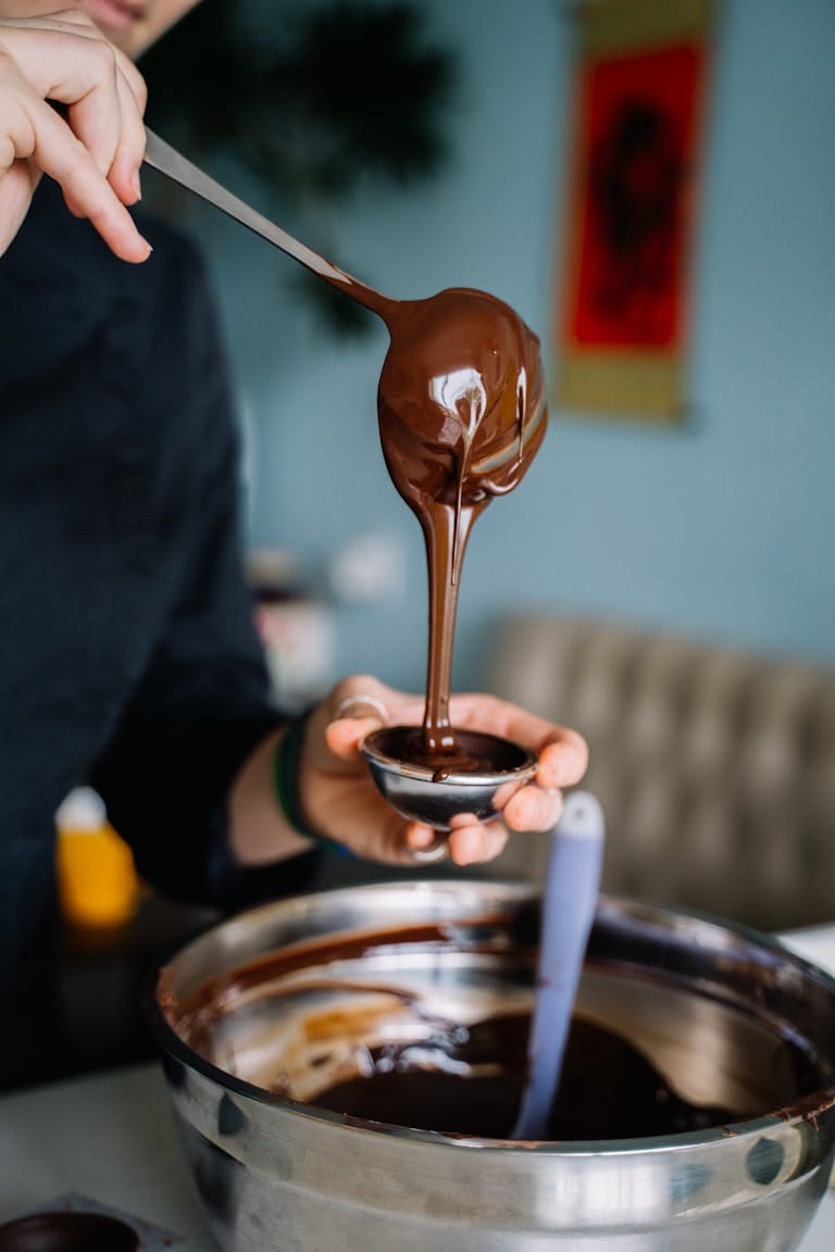 Close-up of chocolate ganache pouring into a container, showcasing culinary detail. | Dietitians Reveal 8 ‘Guilty’ Snacks That Burn Fat (Yes, Chocolate Made the List)
