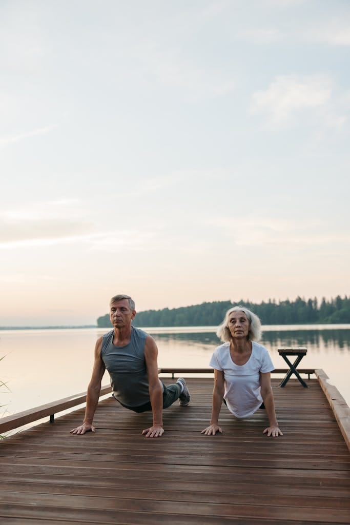 Elderly couple performing yoga outdoors by a serene lake. | Age Reversal Workout: This "Slow-Mo" Method Builds Strength & Fights Muscle Loss (Even at 70+!)