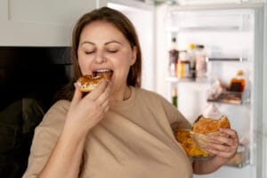 An obese woman eating junk food | The 9 Worst Things to Do Before 9 A.M. If You Want to Burn Fat Faster, According to Dietitians