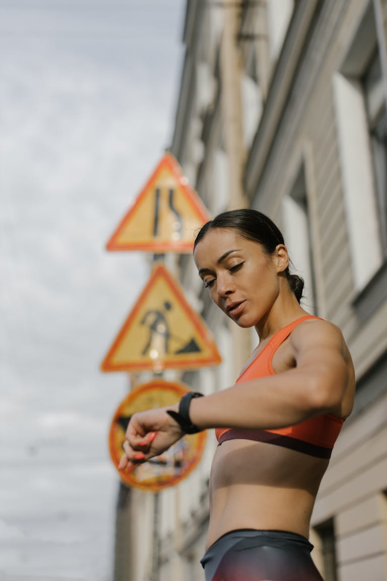 Fit woman in activewear checks her watch on an urban street, embodying fitness and lifestyle. | Think You Don’t Have Time to Strength Train? You’ll Want to See This