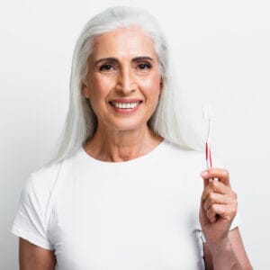 mature woman holding tootbrush | How Your Oral Health Changes as You Age and What to Do to Stay Healthy