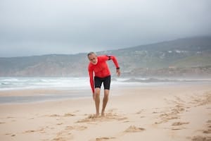 Senior man wearing workout clothes stretching on a sandy Portuguese beach facing the ocean. | Weak Bones? 7 Science-Backed Tips to Boost Bone Density (No Meds Needed)