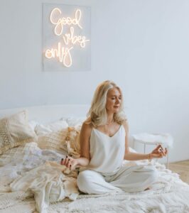 Serene woman meditating on a cozy bed under 'Good Vibes Only' neon sign. | Master Your Morning: 5 Expert Habits for Stable Blood Sugar All Day
