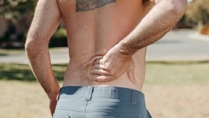Shirtless man holding his lower back outdoors indicating pain or discomfort. | 10 Life-Changing Stretches That Eased My Lower Back Pain in Just Weeks