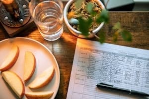 Top view of apple slices, water, and a calorie counter sheet on a wooden table promoting a healthy lifestyle.