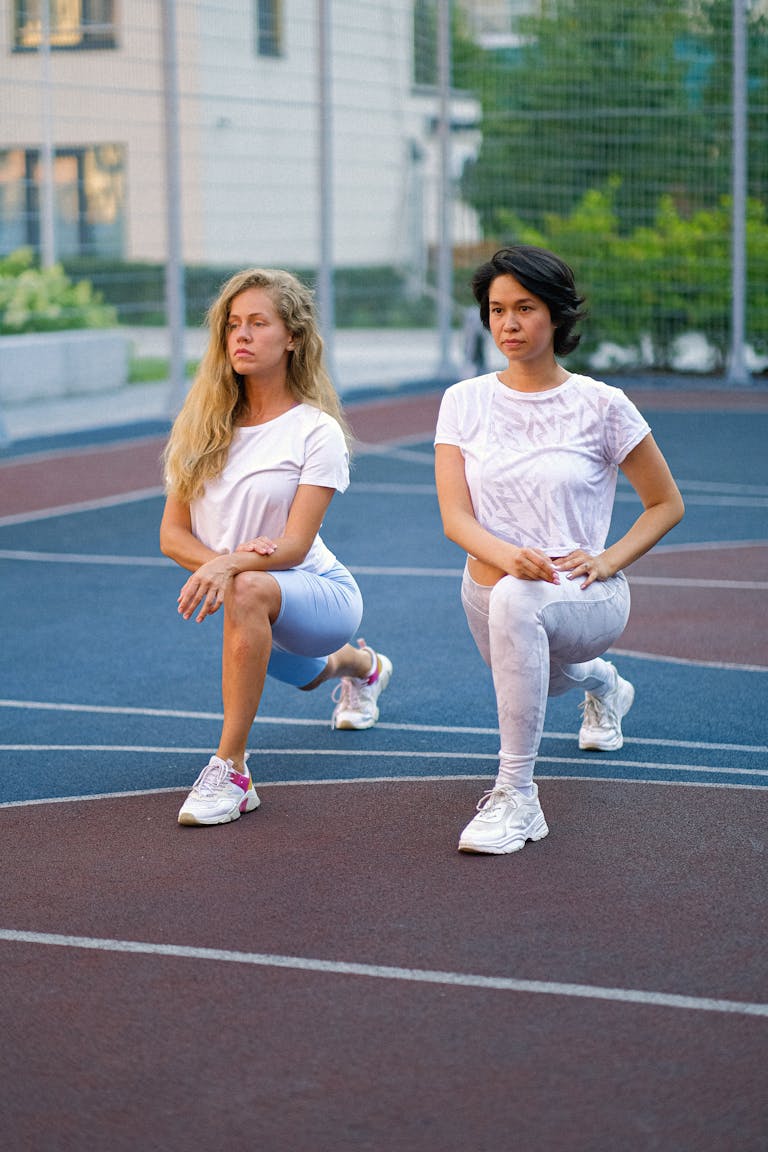 Two women in activewear performing lunges on an outdoor sports court. | This One Exercise Lowers Diabetes Risk More Than Walking, According to a New Study | Trainers Swear by These 8 Beginner Exercises—And They’re Safer Than You Think