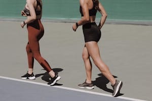 Two women walking on an outdoor track in sportswear, emphasizing healthy lifestyle and fitness. | This 7-Day Walking Plan Burns Fat Fast—And It’s Trainer-Approved