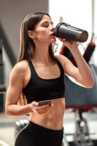woman drinking supplement in the gym | This One Protein Could Be the Key to Burning Dangerous Belly Fat, Say Dietitians | Why You're NOT Losing Fat: 10 Common Daily Habits Undermining Your Progress (Expert Reveals All)