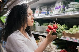 Woman in grocery store choosing fresh radishes from the vegetable aisle. | 10 Popular Vegetables That Aren’t as Good for You as You Think (And 10 Smarter Swaps)