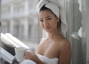 Woman in towel sipping coffee and reading a book indoors, exuding a sense of relaxation. | Psychologists Say These 9 Daily Habits Are the Secret to Looking 20 Years Younger