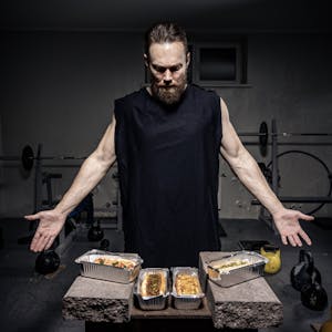 A bearded man in a gym presents nutritious meals in aluminum pans. | Boost Your Gym Workout: The 12 Pre-Workout Foods for Peak Performance (And 3 That Kill Your Gains!)