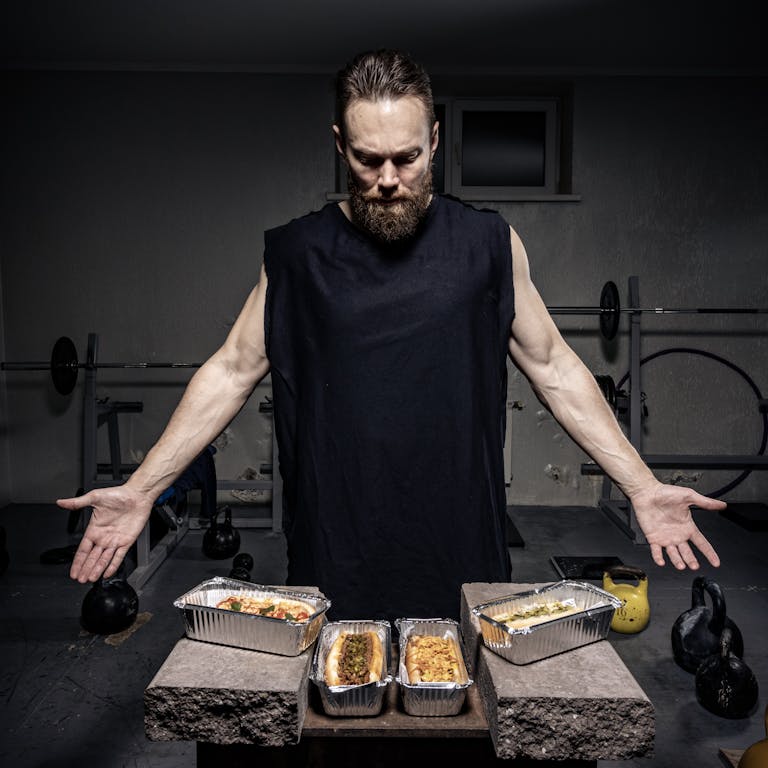 A bearded man in a gym presents nutritious meals in aluminum pans. | Boost Your Gym Workout: The 12 Pre-Workout Foods for Peak Performance (And 3 That Kill Your Gains!)