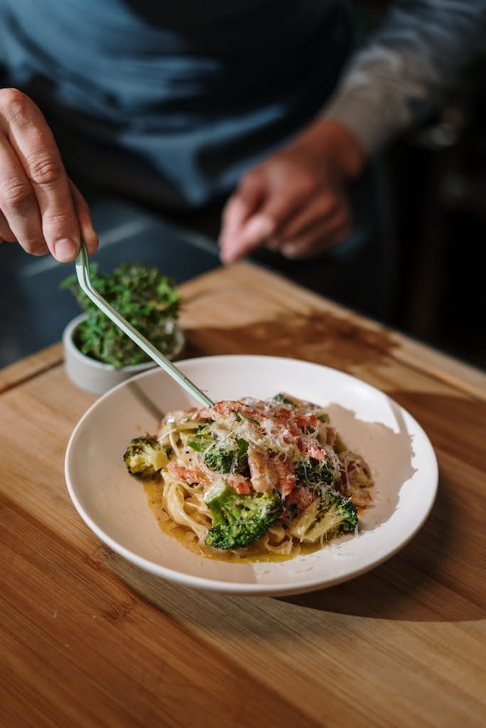 A delicious plate of Italian pasta garnished with fresh herbs and broccoli, prepared by a male chef. |