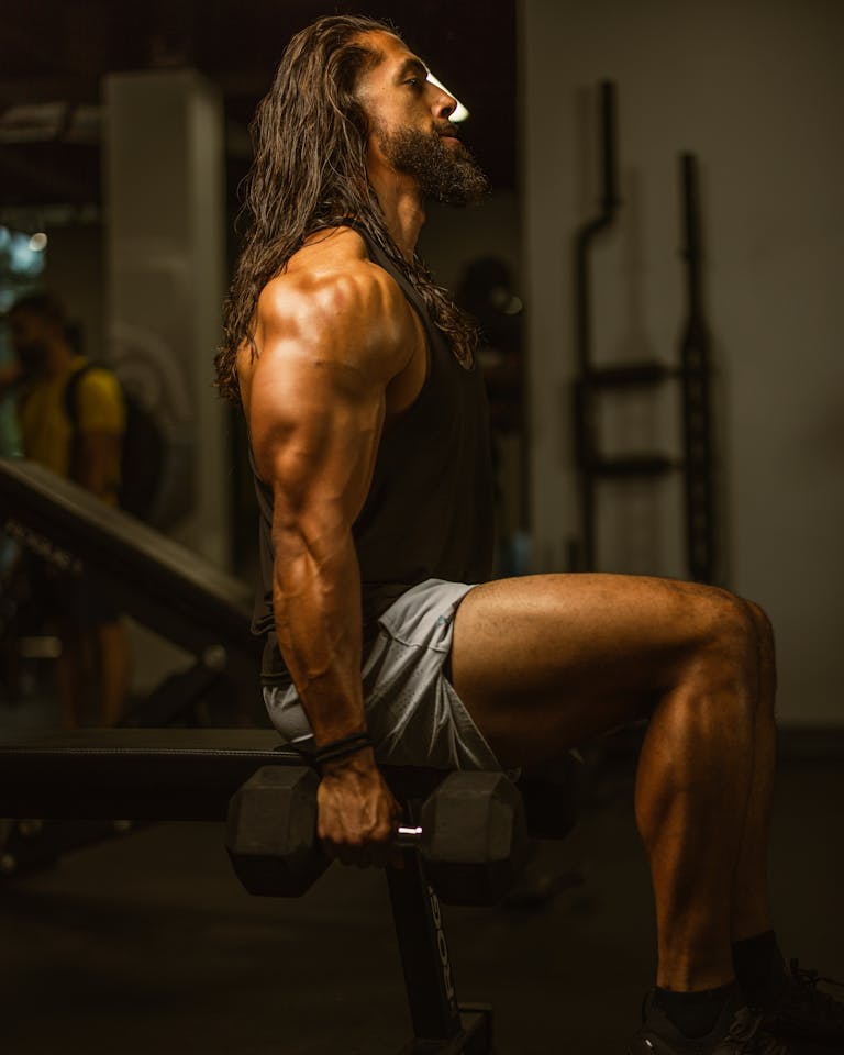 A muscular man works out with dumbbells in a gym, showcasing strength and dedication. | STOP Wasting Workouts! These 5 Compound Exercises Build Incredible Full-Body Strength & Muscle FASTER