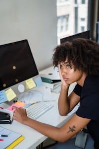 A woman looks tired while sitting at her work desk surrounded by computers and paperwork. | Tired All the Time? This Powerhouse Supplement Boosts Focus, Stamina & Overall Vitality