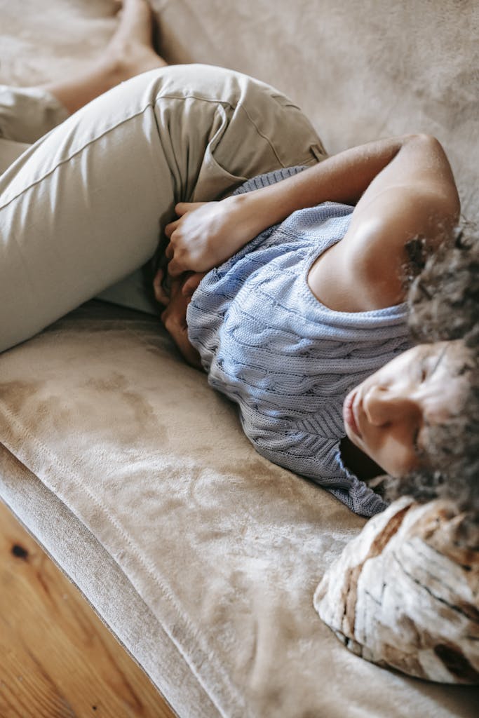 A young woman lying on a couch holding her stomach, indicating pain or discomfort. | The Silent Gut Destroyers: 4 Hidden Ingredients in Your Favorite Processed Foods (Avoid Them NOW!)