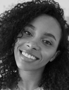 Black and white portrait of a smiling woman with curly hair, showcasing natural beauty.