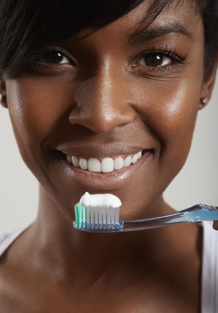 black woman brushing her teeth | I Asked 5 Cosmetic Dentists Which Toothpastes Work Best for Whitening—Did Yours Make the List?