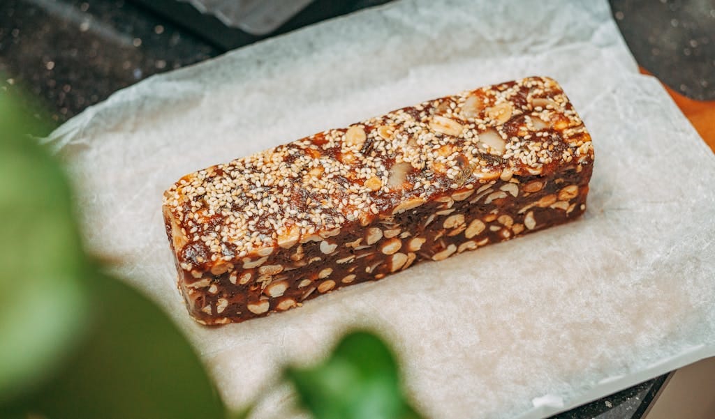 Close-up image of a nut and sesame seed protein bar on parchment paper, ideal for healthy snacking. | Stop Cravings Cold! The 10 "Clean" Protein Bars That Actually Keep You Full (Trainer Approved!)