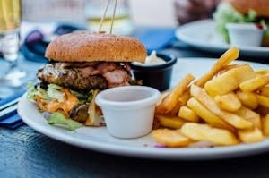 Close-up of a juicy burger and crispy fries served with sauces, perfect for a hearty meal. | STOP Eating These! 10 Foods Destroying Your Skin (And 10 Superfoods for a Flawless Complexion)