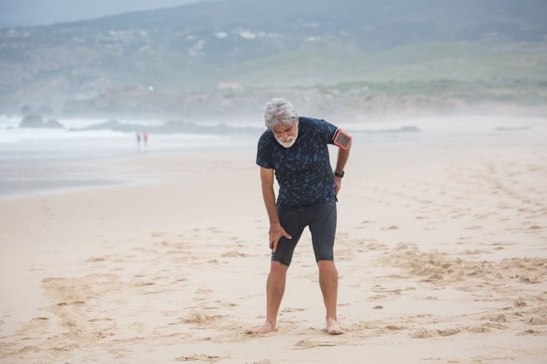 Elderly man stretching on a sandy beach in Portugal, promoting healthy lifestyle. | The "Age Test" Experts Use: If You Struggle With These 5 Movements, You're Aging Faster Than You Think