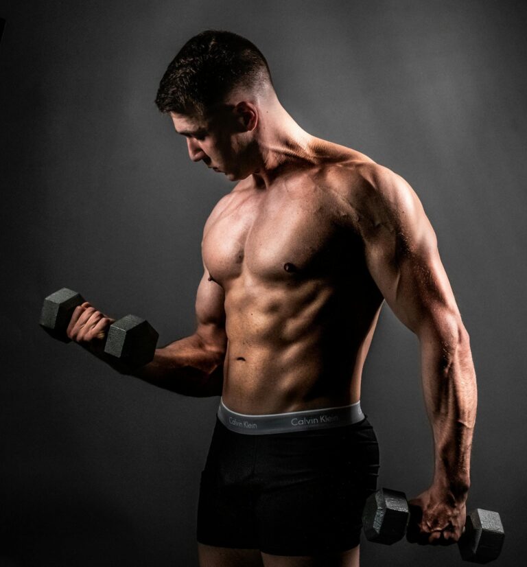 Fit shirtless man lifting dumbbells in a studio, showcasing his muscles and fitness. | Strength Training Timing: How Long Before You See Real Gains?
