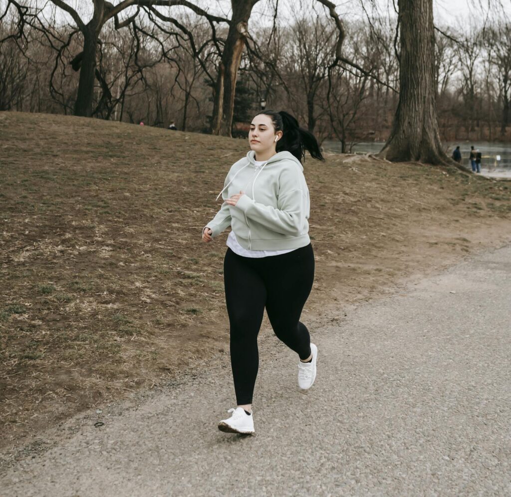Full body motivated plus sized female in gray hoodie running in autumn park