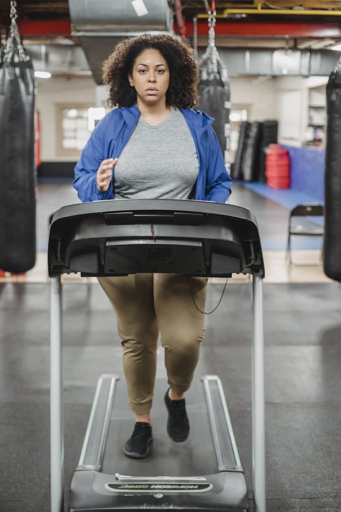 Full body of overweight female running on treadmill during workout and looking at camera | Reclaim Your Power: The Gentle Walking Plan for Plus-Size Bodies (Boost Energy & Shed Pounds Effortlessly!)