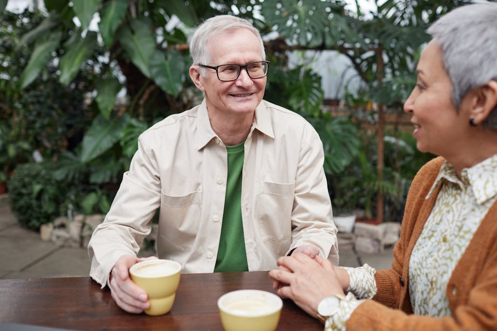 Happy senior couple sharing coffee and conversation in a lush garden setting. | Defy Your Age: 75-Year-Olds Reveal Their Everyday Habits for Peak Energy & a Brilliant Mind