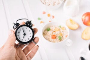 a hand holding a stop watch next to a plate of food. The image is use to represent intermittent fasting
